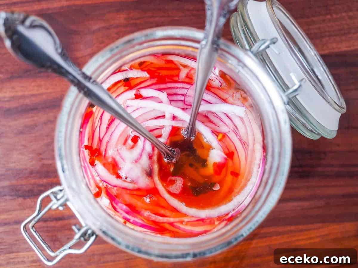 Quick Pickled Red Onions Recipe for Toppings & Salads 10 A close up of a glass jar of red onions with two small forks in it.