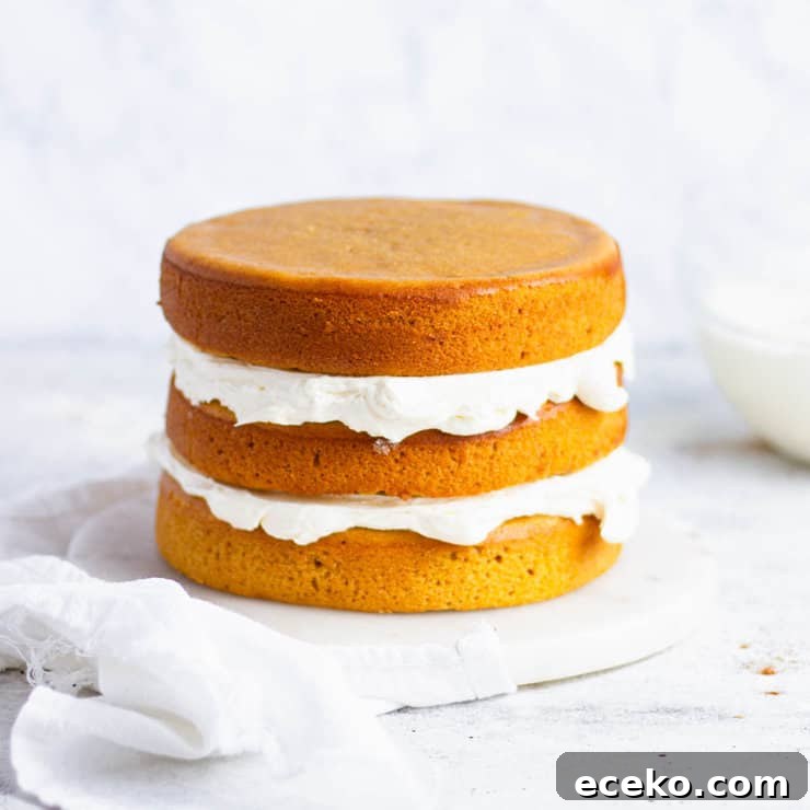 Layers of orange sweet potato cake filled with frosting next to a clear bowl of white frosting.