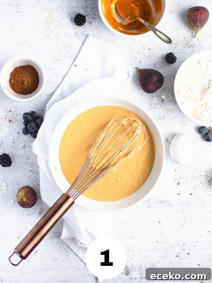 Overhead view of sweet potato cake batter in a white bowl with a copper whisk.