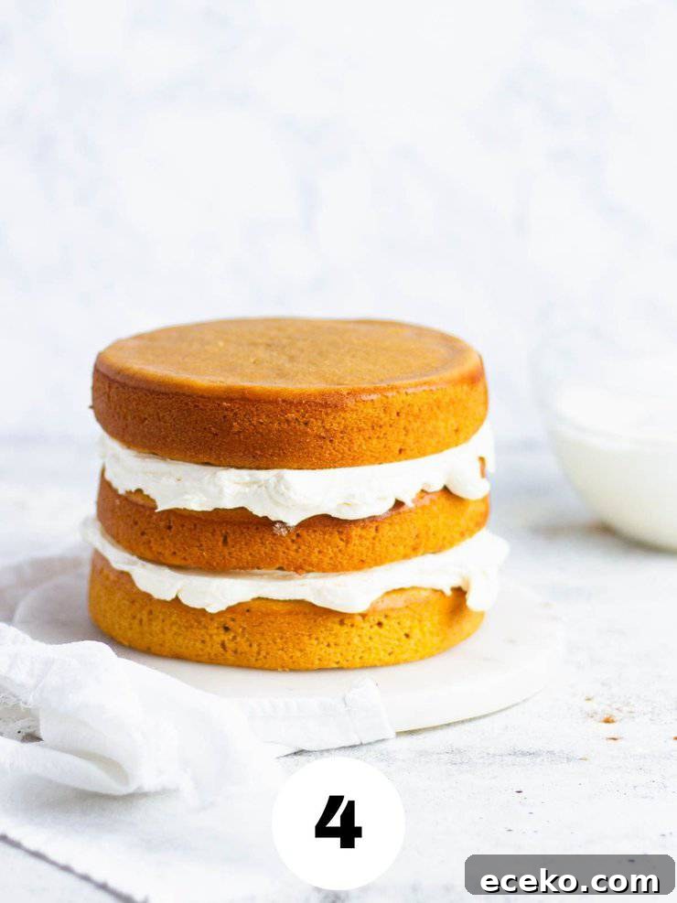Layers of orange sweet potato cake filled with frosting next to a clear bowl of white frosting.