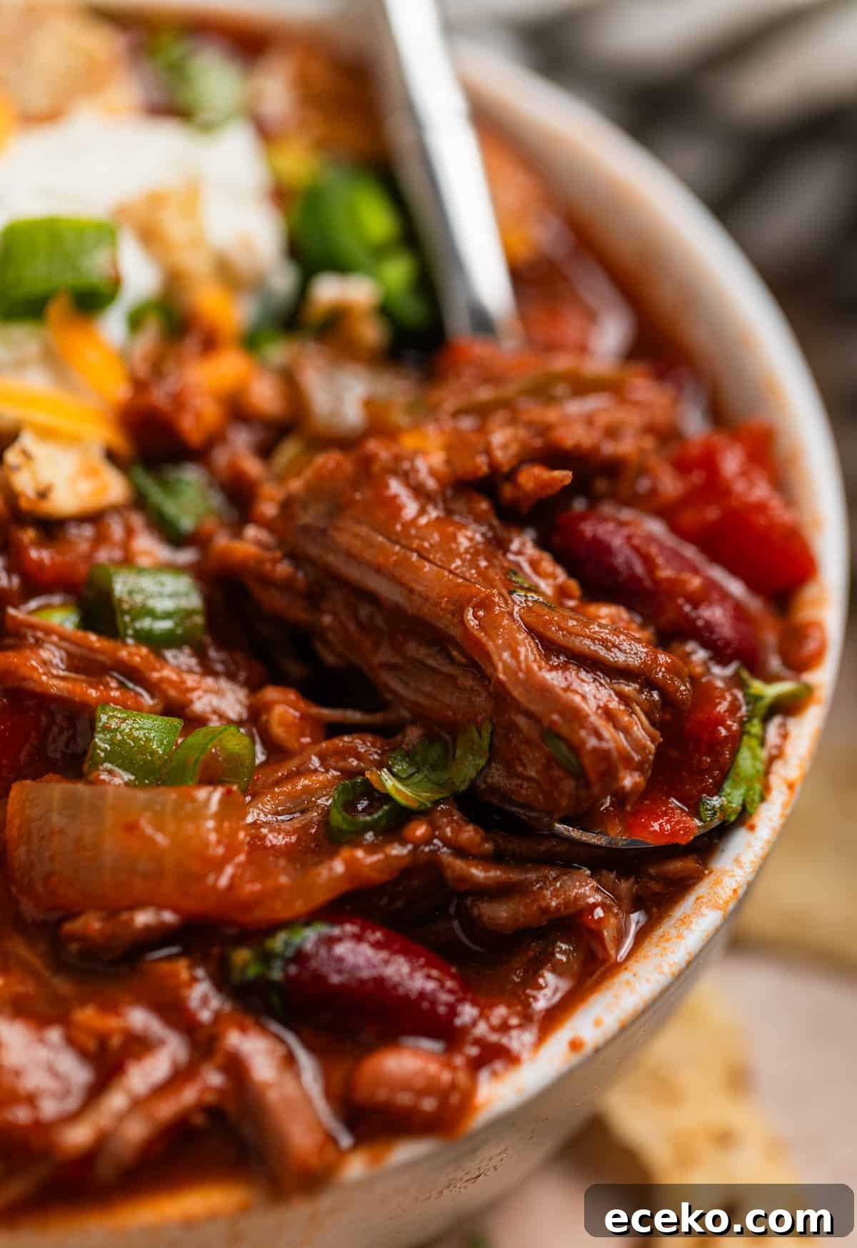Bowl of shredded beef chili with spoon scooping into it.