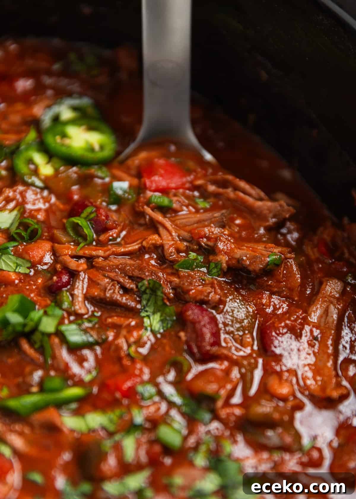 Slow cooker shredded beef chili in crockpot topped with cilantro and jalapeño with ladle.