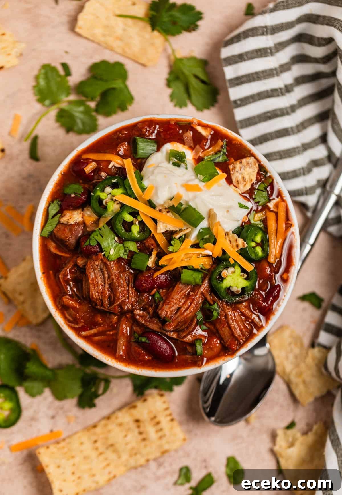 Overhead view of chili in bowl topped with sour cream, cheese, cilantro and other toppings.