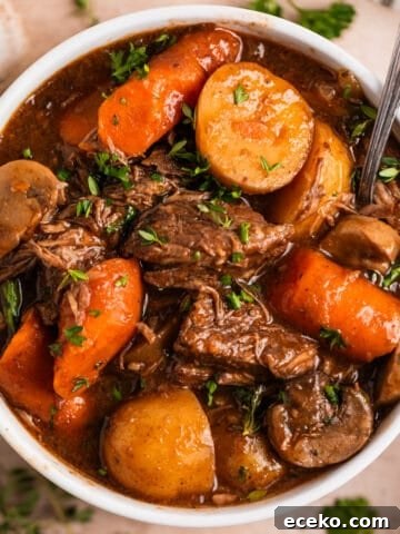 White bowl with crockpot beef stew with mushrooms, carrots and potatoes topped with chopped parsley.