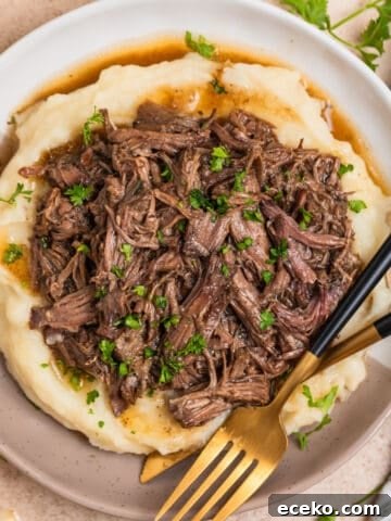 Tan and white plate with crock pot shredded beef over mashed potatoes.