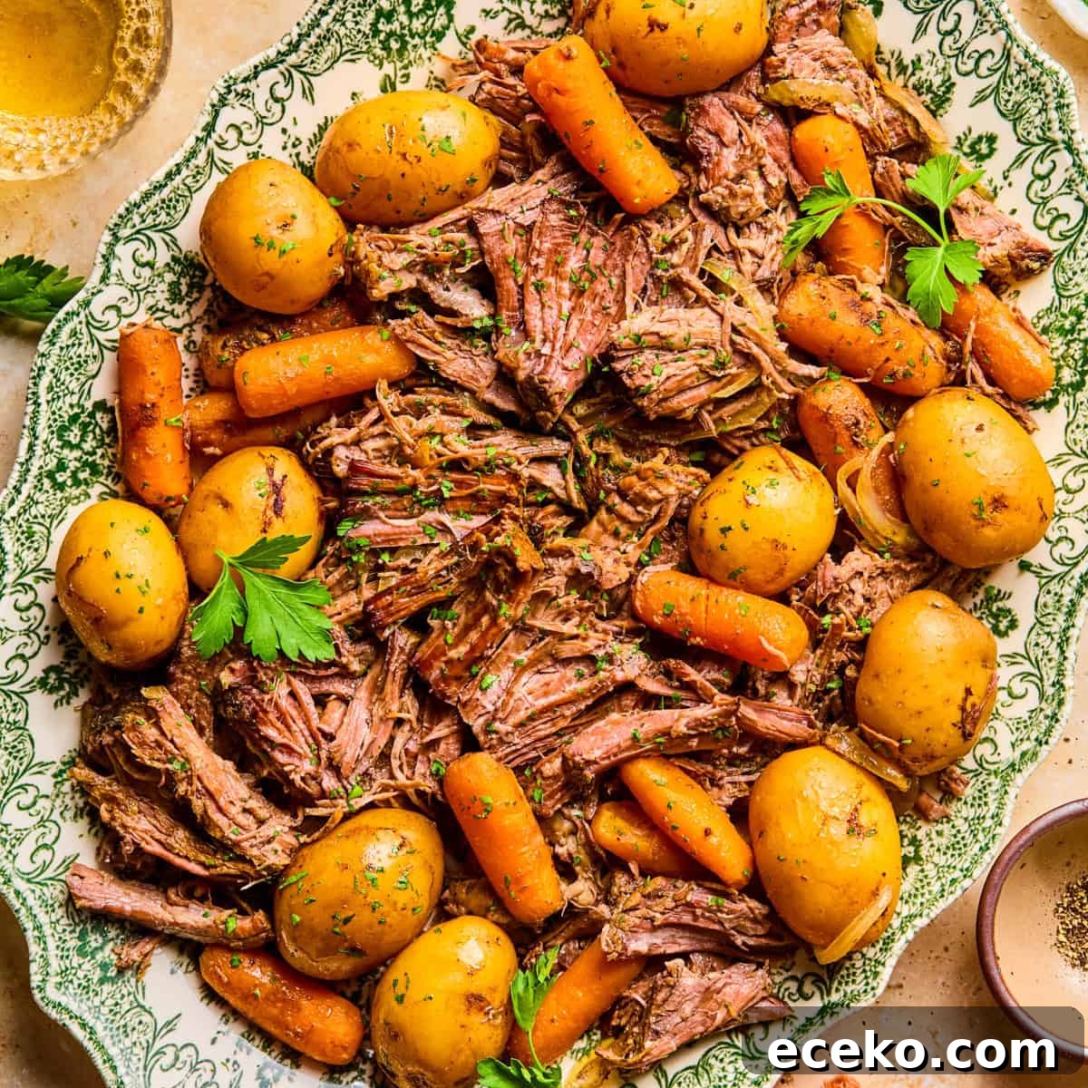 Plate with pot roast served with meat, potatoes and carrots and chopped parsley on top.
