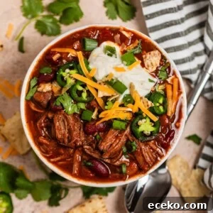 Overhead view of shredded beef chili topped with sour cream, cilantro, cheese and more.