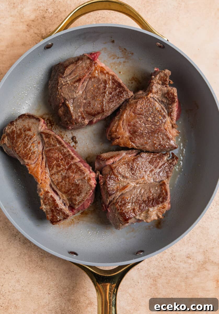 Seared chuck roast pieces in skillet being browned.