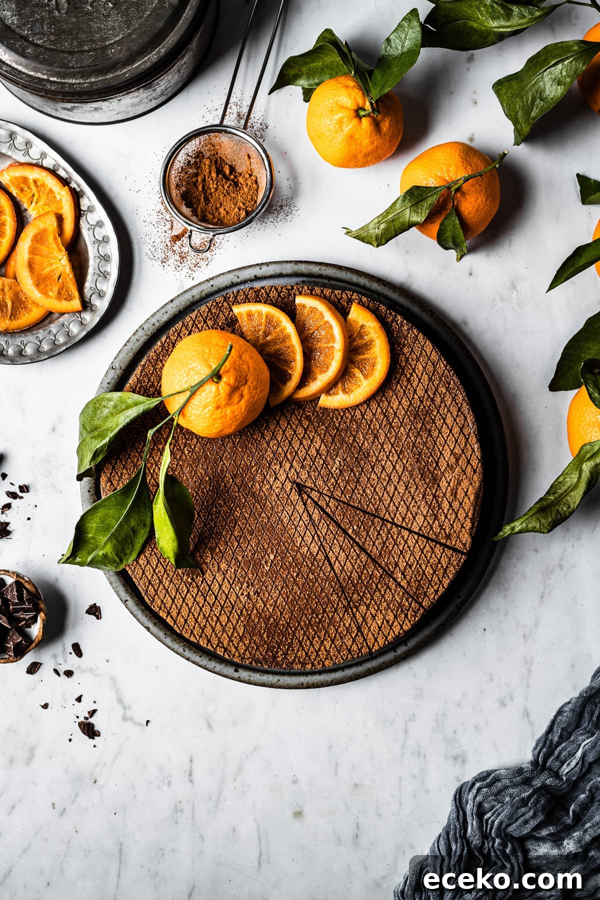 A chocolate orange cheesecake decorated with cocoa stencil, orange slices and a whole orange.