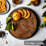 A chocolate orange cheesecake decorated with orange slices and a whole orange with a few slices removed, on a white marble surface.