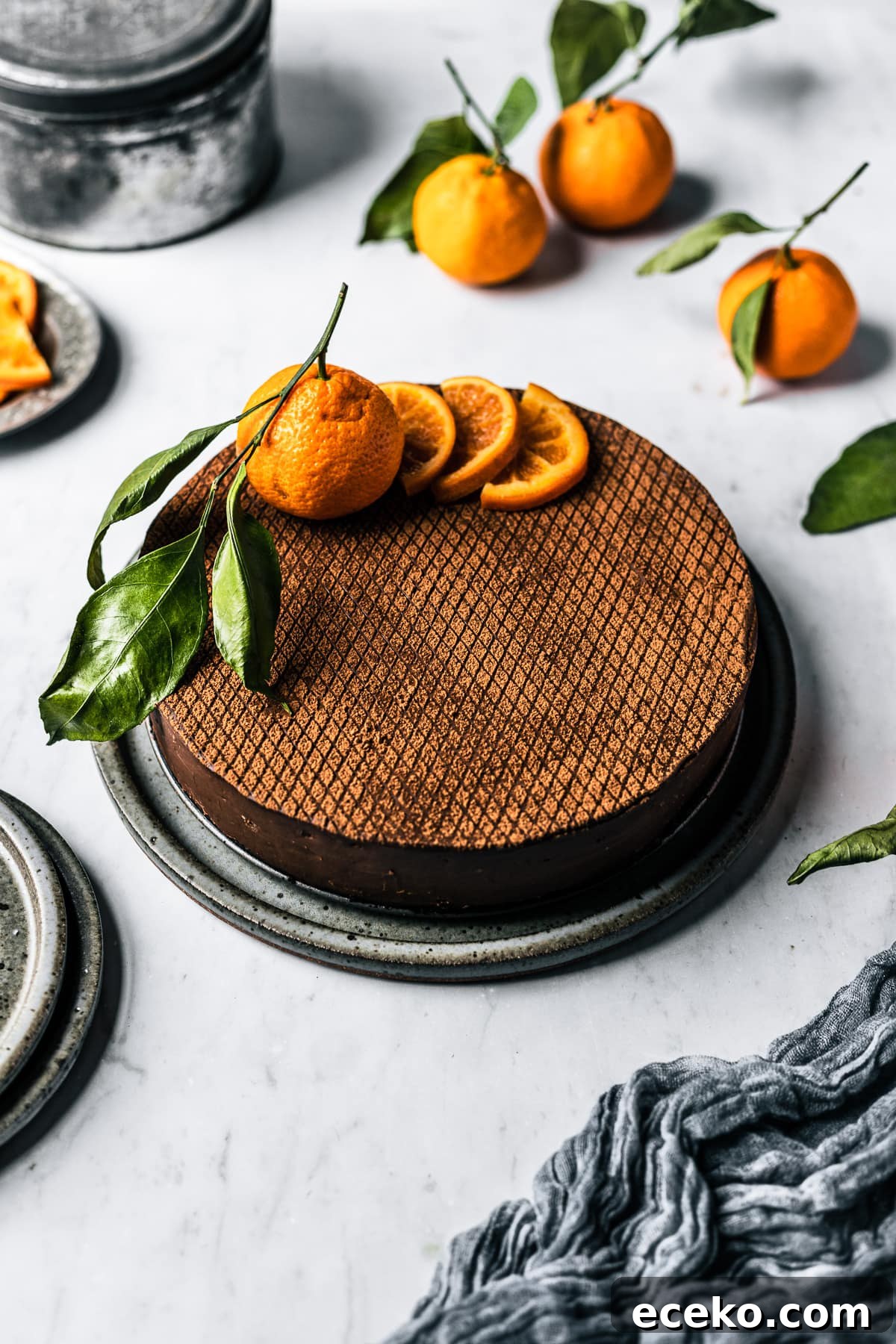 A chocolate cheesecake with cocoa stencil, dried oranges and a whole orange on top.