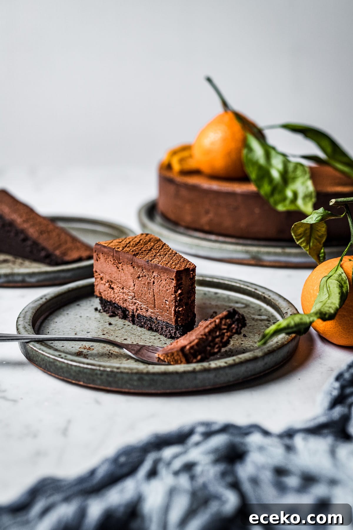 A slice of orange chocolate cheesecake on a ceramic plate with a bite resting on a fork.