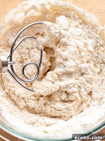 A glass bowl with a sourdough starter and danish dough whisk mixing it together.