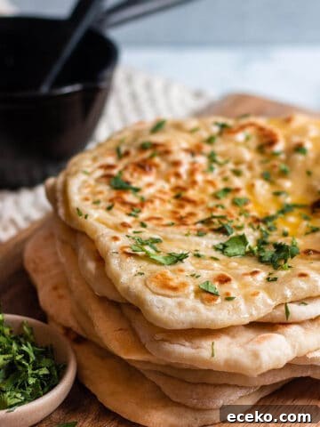 Stack of sourdough naan on a wood board with cilantro and cast iron butter melter.
