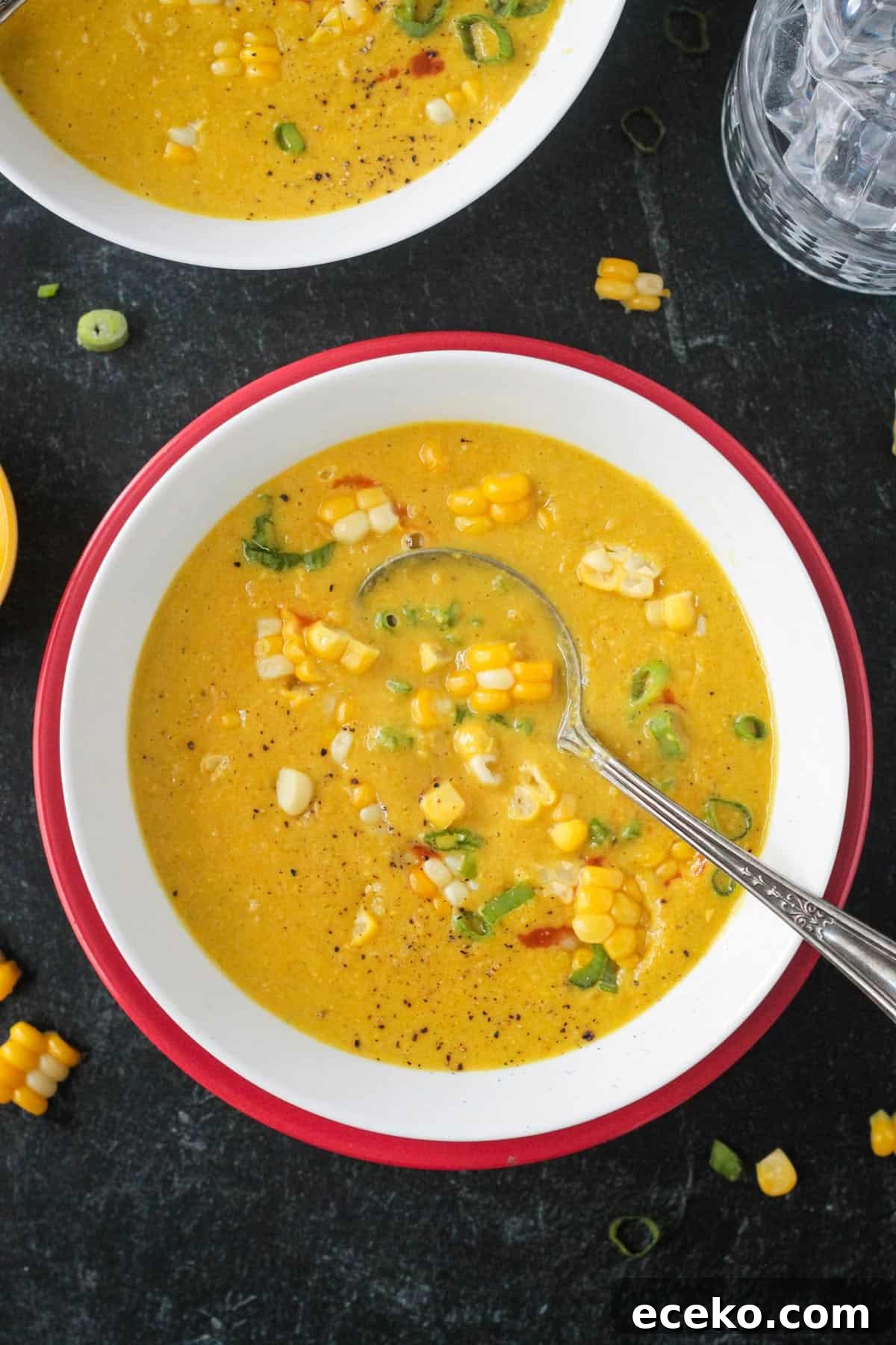 Creamy Coconut Curry Corn Soup Recipe 2 Creamy curried corn soup in a white bowl on a red plate.