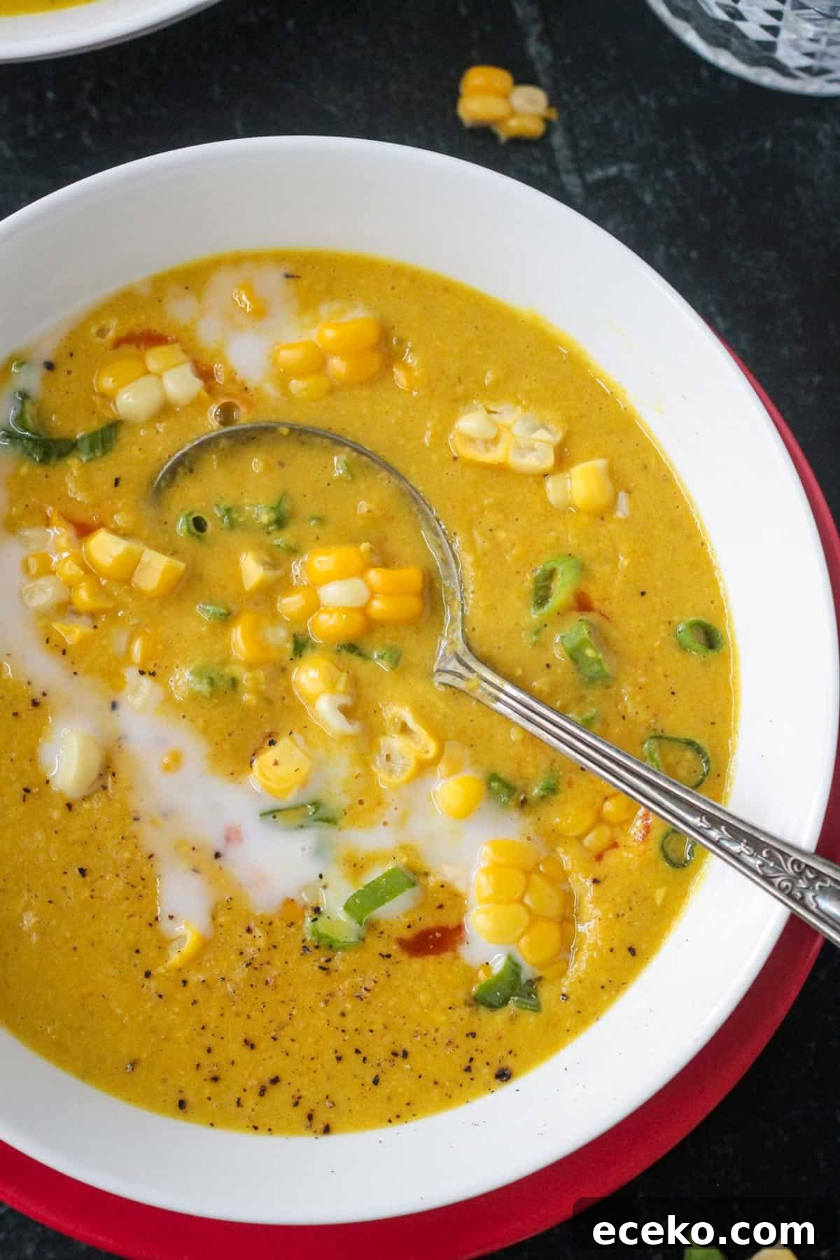 Creamy Coconut Curry Corn Soup Recipe 12 Close up overhead view of a bowl of creamy curried corn soup garnished with corn kernels, sliced green onions, and a drizzle of coconut milk.