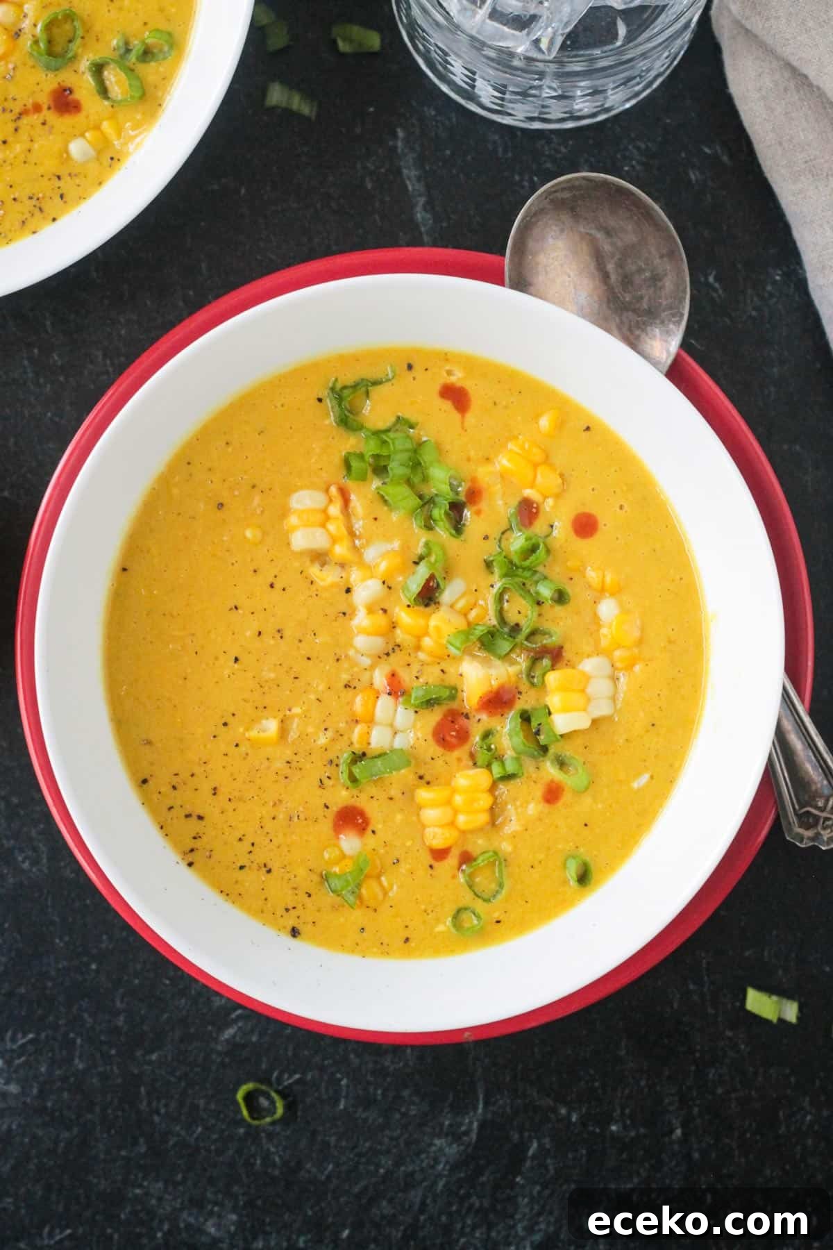 Creamy Coconut Curry Corn Soup Recipe 9 Golden yellow soup garnished with corn, green onions, and hot sauce.