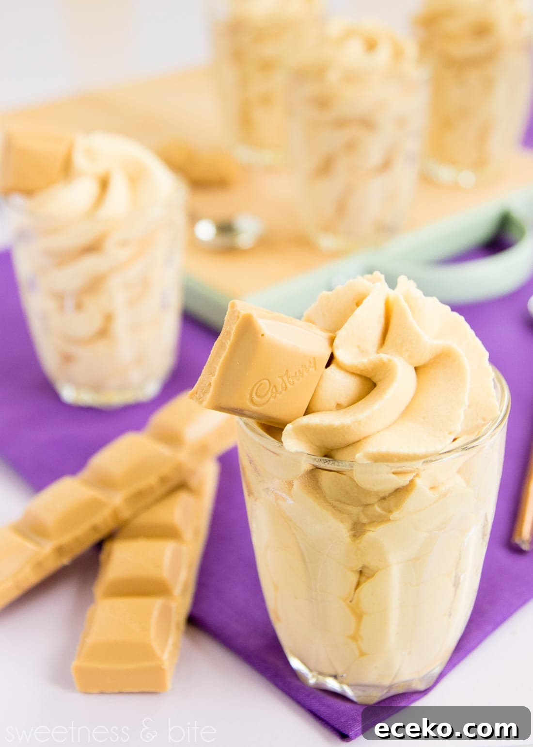 Caramilk mousse piped into a small glass with a square of Caramilk chocolate on top and two rows of chocolate in the background.