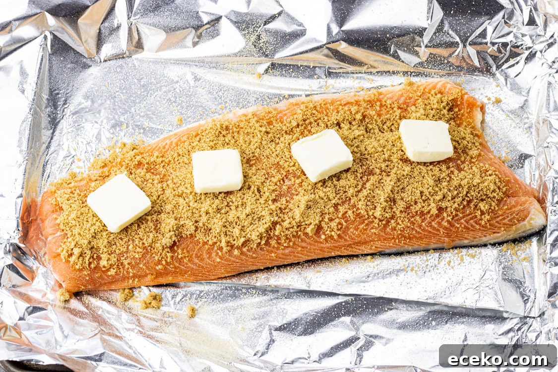 salmon filet on a piece of foil, topped with brown sugar and butter slices