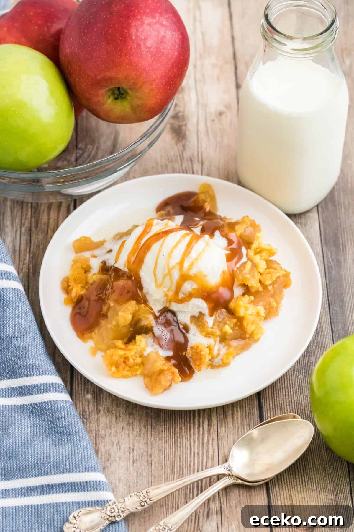 3-Ingredient Apple Dump Cake Recipe: Quick Crowd-Pleasing Dessert 9 Apple dump cake topped with vanilla ice cream and caramel sauce. Glass of milk and apples are next to plate.