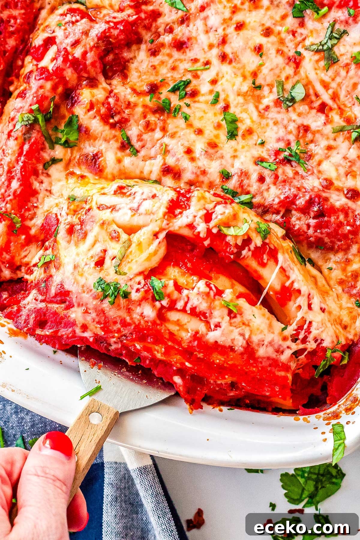 Three-Cheese Manicotti with Homemade Tomato Sauce 11 A close-up shot of a spatula lifting a cheesy manicotti roll out of the baking dish, revealing the saucy layers and creamy interior.