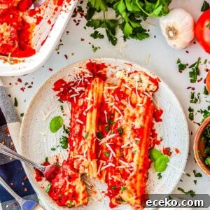 Three-Cheese Manicotti with Homemade Tomato Sauce 12 A plated serving of two manicotti rolls covered in red sauce and cheese, cut open with a fork to show the white ricotta filling inside.