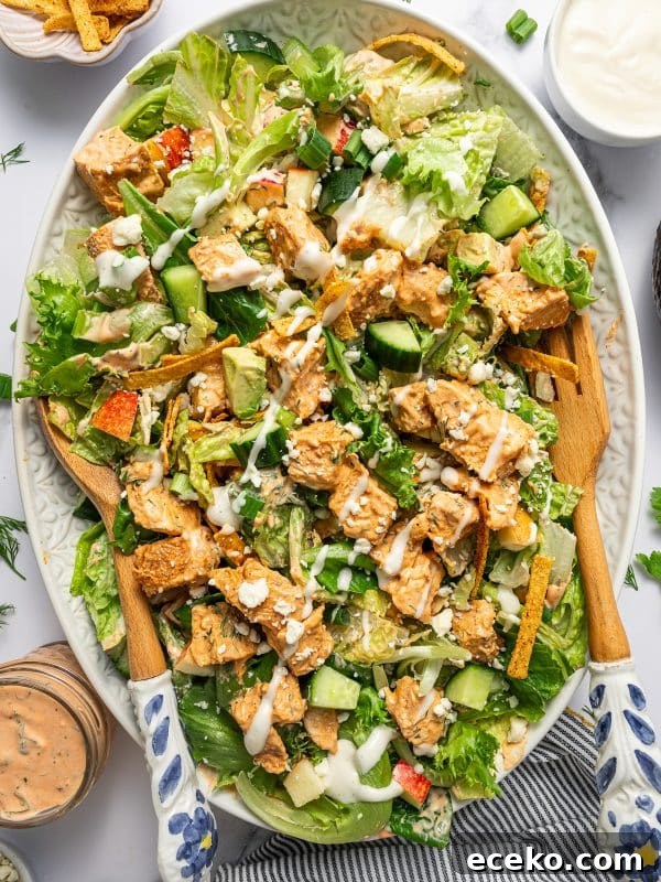 Crispy Homemade Croutons Recipe for Salads and Soups 7 Close-up of tossed buffalo chicken salad on a light green oval platter with chopped lettuce, cucumber, avocado, apple, tortilla strips, green onions, buffalo chicken, blue cheese crumbles, creamy buffalo dressing, and ranch dressing.