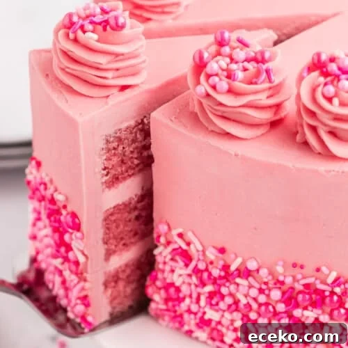 A pink cake with a slice being served out of it. The pink cake is decorated with sprinkles.