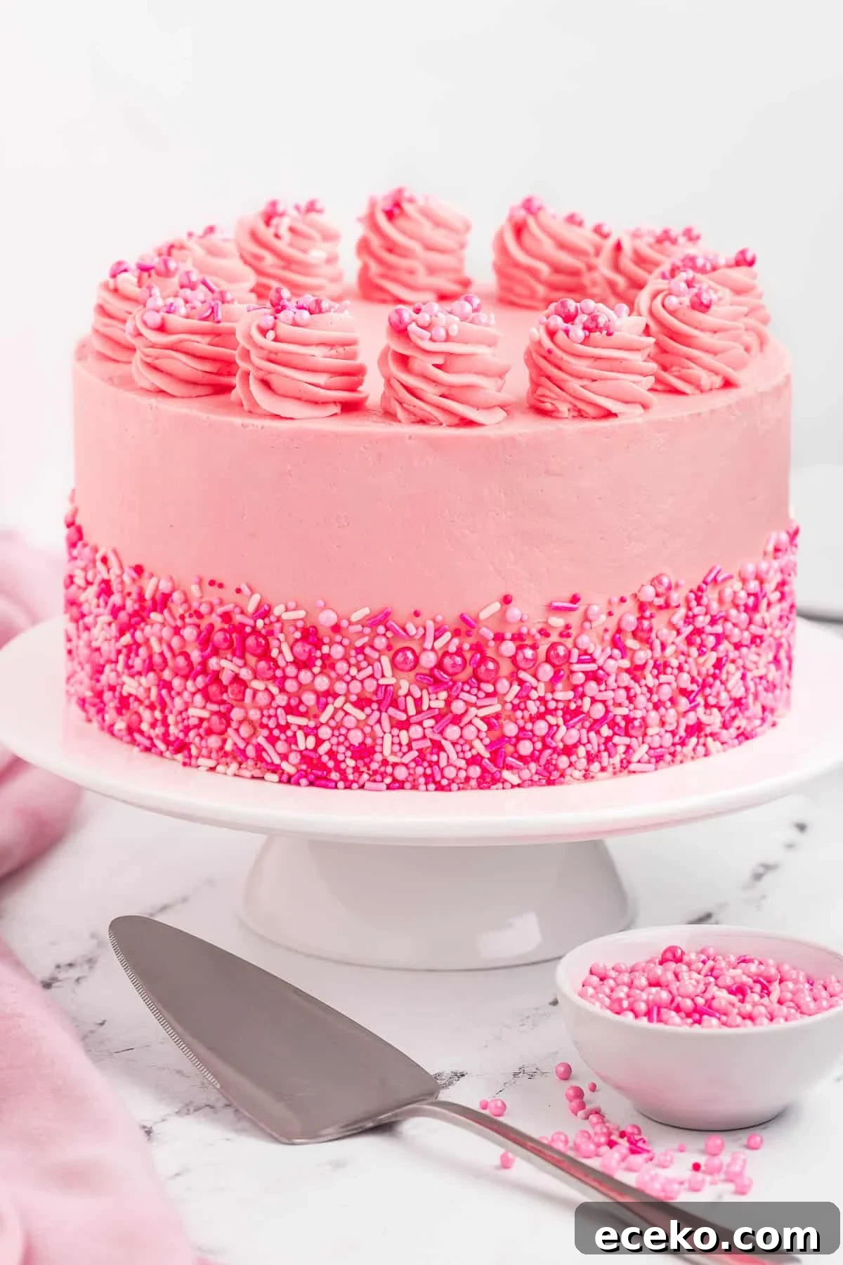 A pink velvet cake on a pedestal decorated with sprinkles.