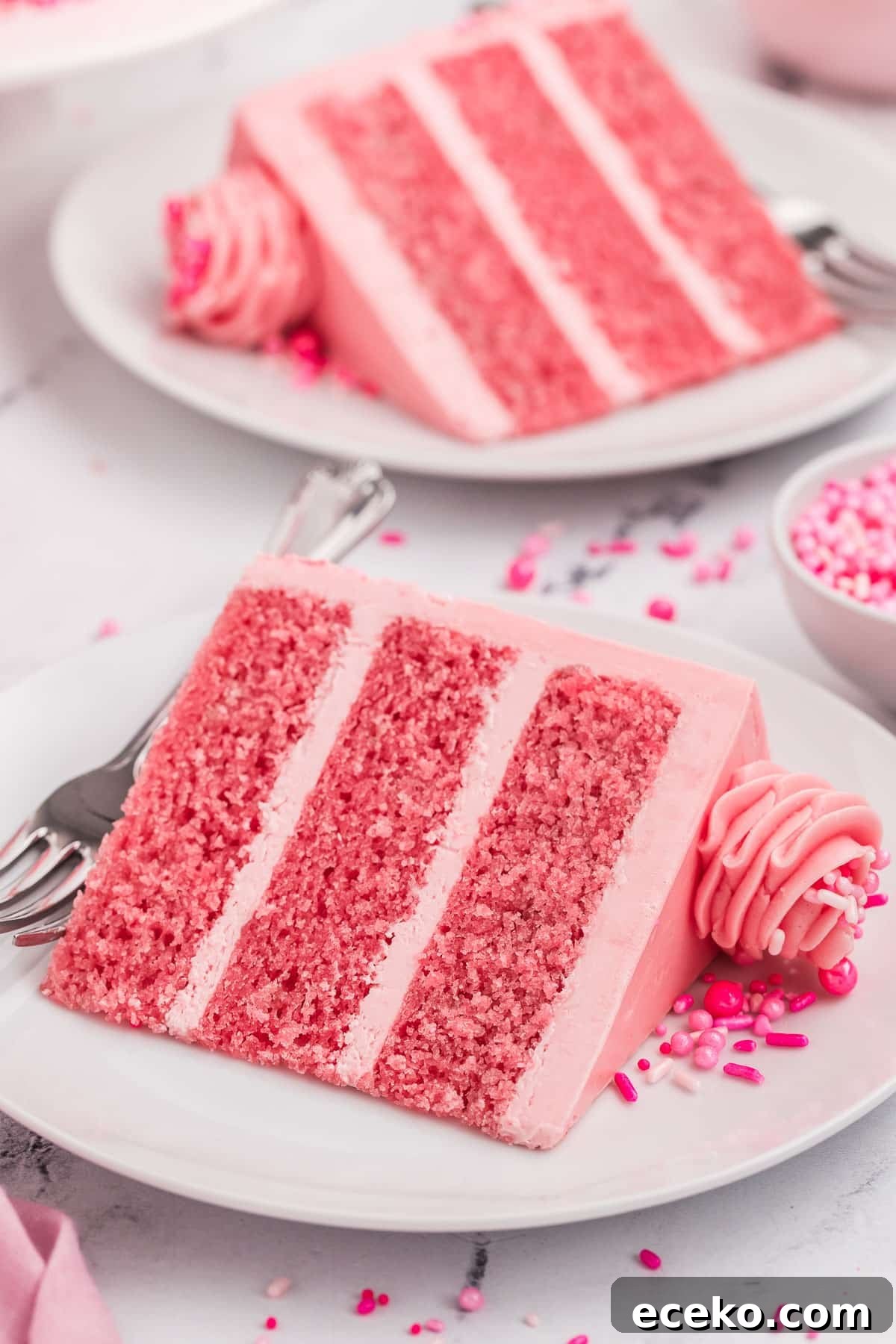 Slices of pink cake on plates with sprinkles on top.