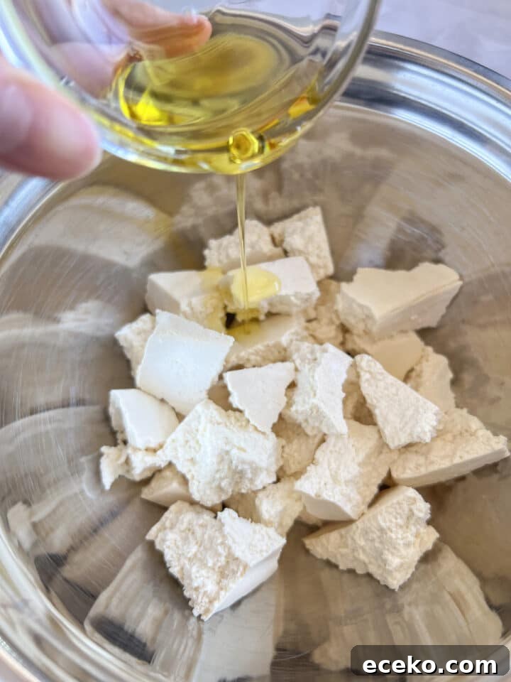 Crispy Air Fryer Tofu Nuggets — Quick Weeknight Recipe 7 Oil being poured over raw tofu chunks in a mixing bowl
