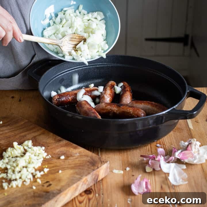Cowboy Stew Recipes: Campfire, Stovetop, Oven & Slow Cooker Methods 5 woamns hands tipping chopped onions from a blue bowl into a black cast iron pan of cooked sausages