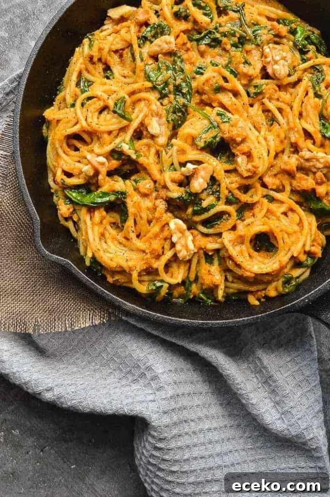 20-Minute Creamy Vegan Pumpkin Pasta Recipe 2 Top down view of pan full of orange spaghetti, walnuts and spinach on a grey teatowel