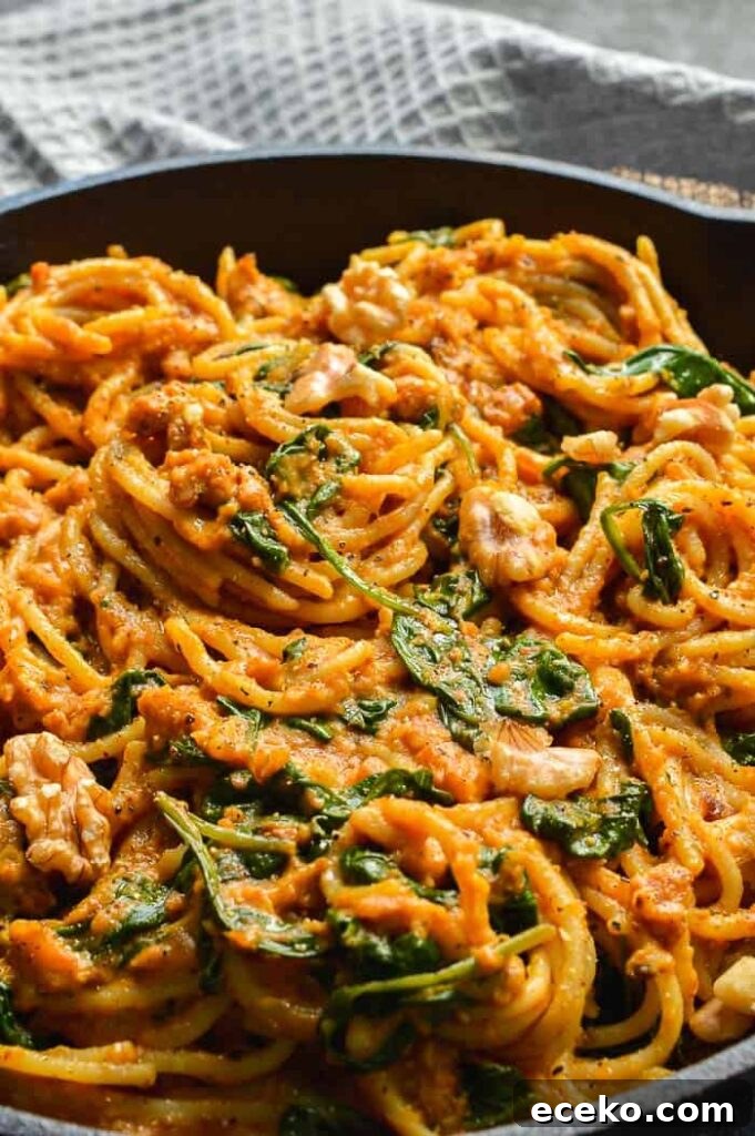 20-Minute Creamy Vegan Pumpkin Pasta Recipe 7 A black cast iron pan with spaghetti in orange sauce with spinach