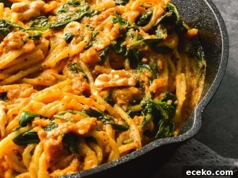 A black pan with spaghetti tossed in creamy pumpkin sauce mixed with spinach and walnuts
