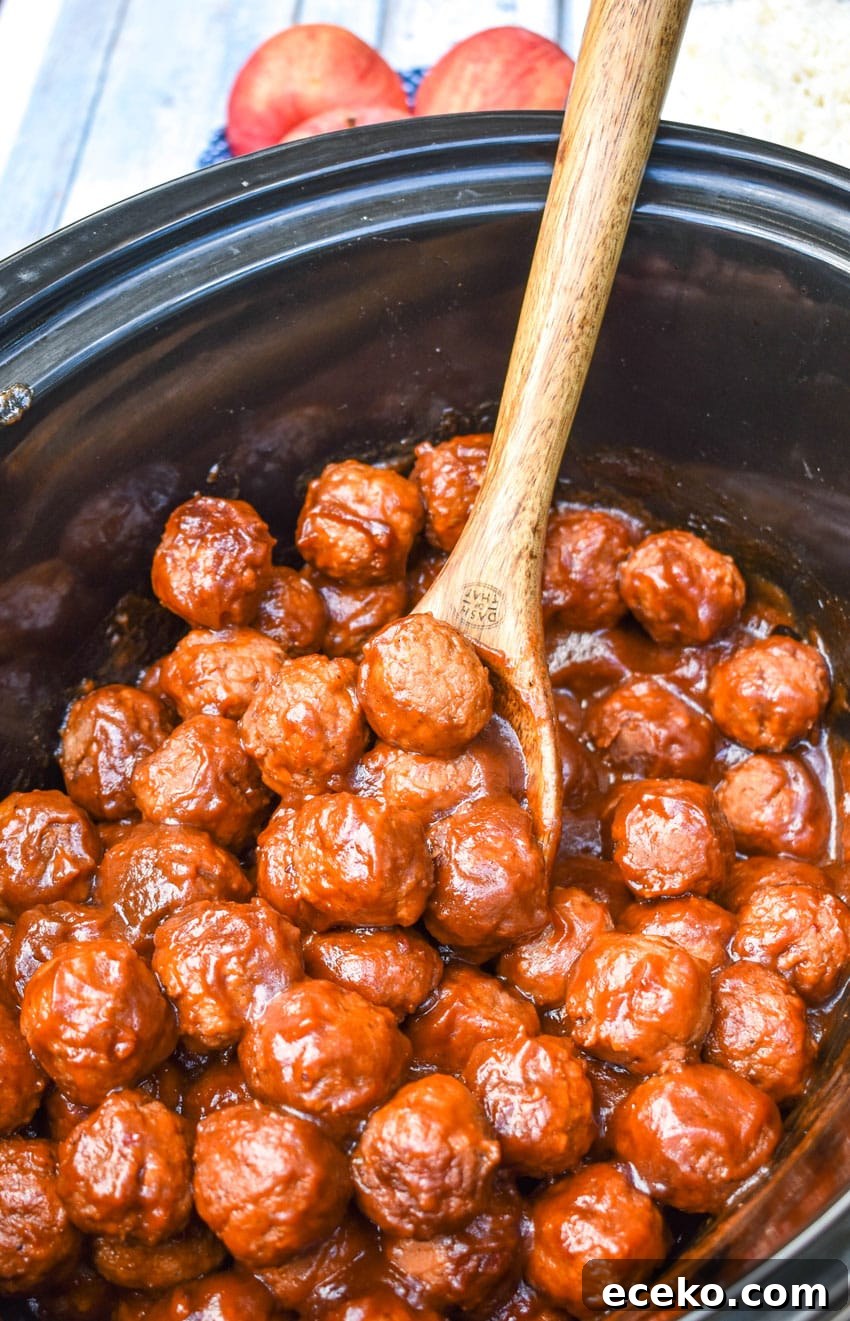 Slow Cooker Apple Butter Meatballs: Sweet Savory Dinner Recipe 5 a wooden spoon scooping apple butter meatballs out of a black crockpot