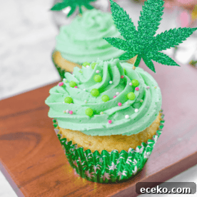 A white countertop with a cutting board and a cannabis cupcake topped with green frosting