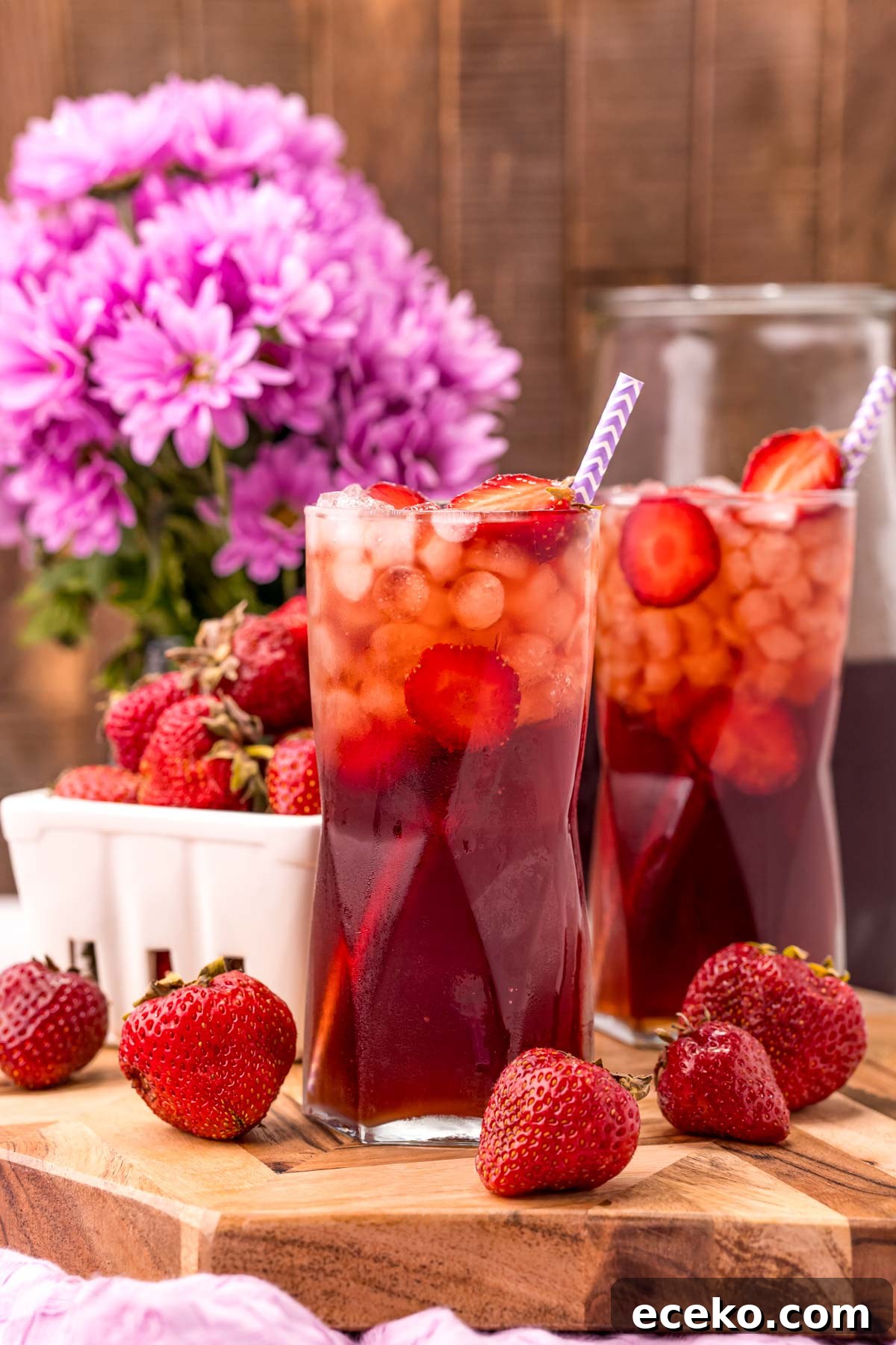 Refreshing Iced Strawberry Tea Recipe for Summer Infusions 3 Photo of two glasses on strawberry sweet tea on a wooden board with strawberries scattered around and purple flowers in the background.