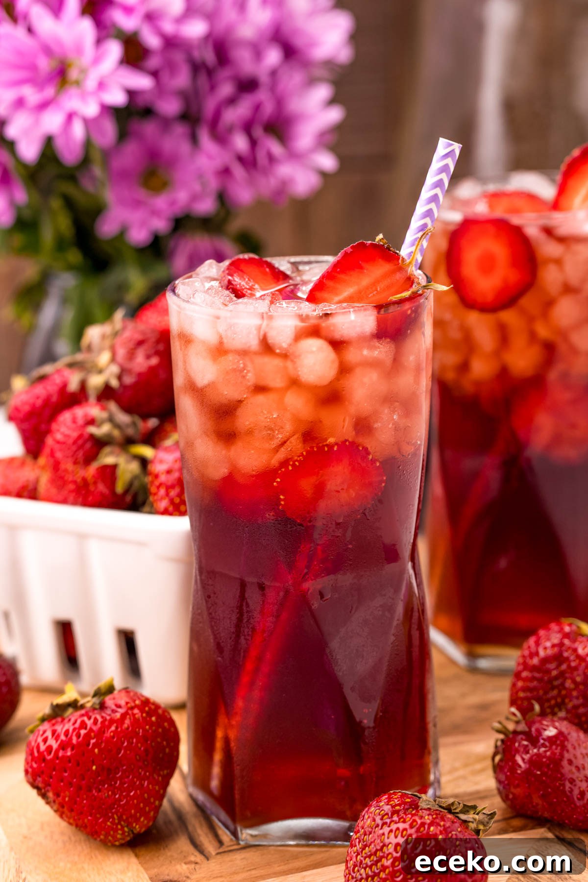 Refreshing Iced Strawberry Tea Recipe for Summer Infusions 6 Close up photo of a glass of strawberry tea with another glass and a carton of strawberries in the background.