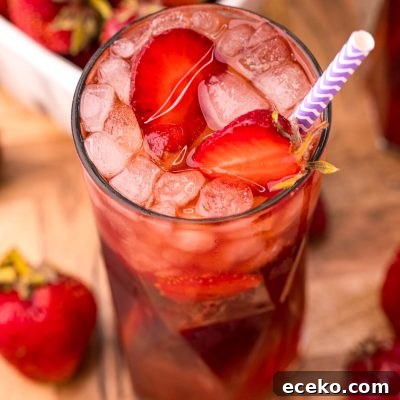 Refreshing Iced Strawberry Tea Recipe for Summer Infusions 7 Close up photo of a glass of strawberry sweet tea on a wooden board with strawberries scattered around.