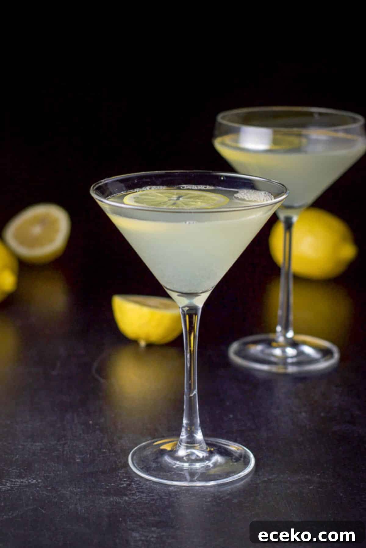 A classic martini glass filled with the lemon drink with the curved martini glass and lemons in the background