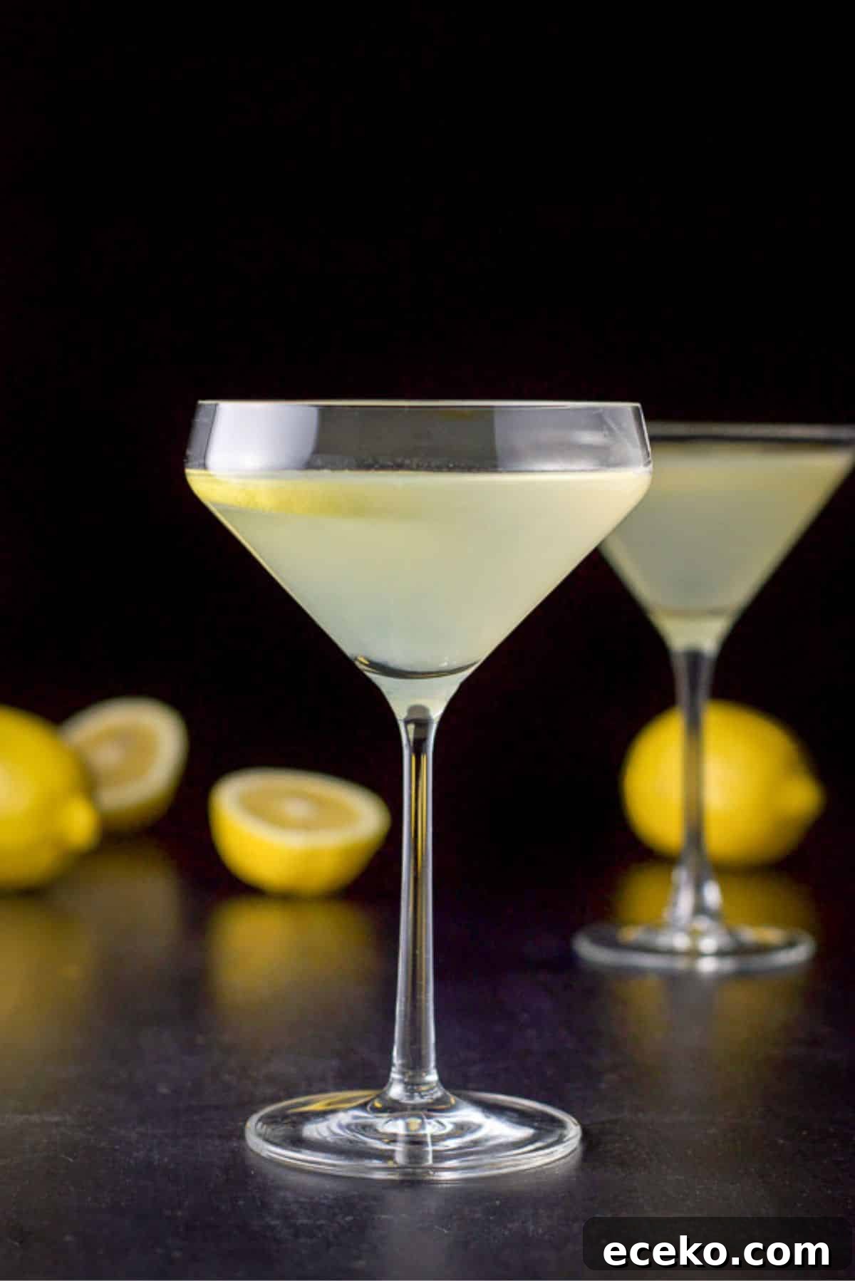 Curved martini glass in vertical view with the cocktail in it with lemons on the table