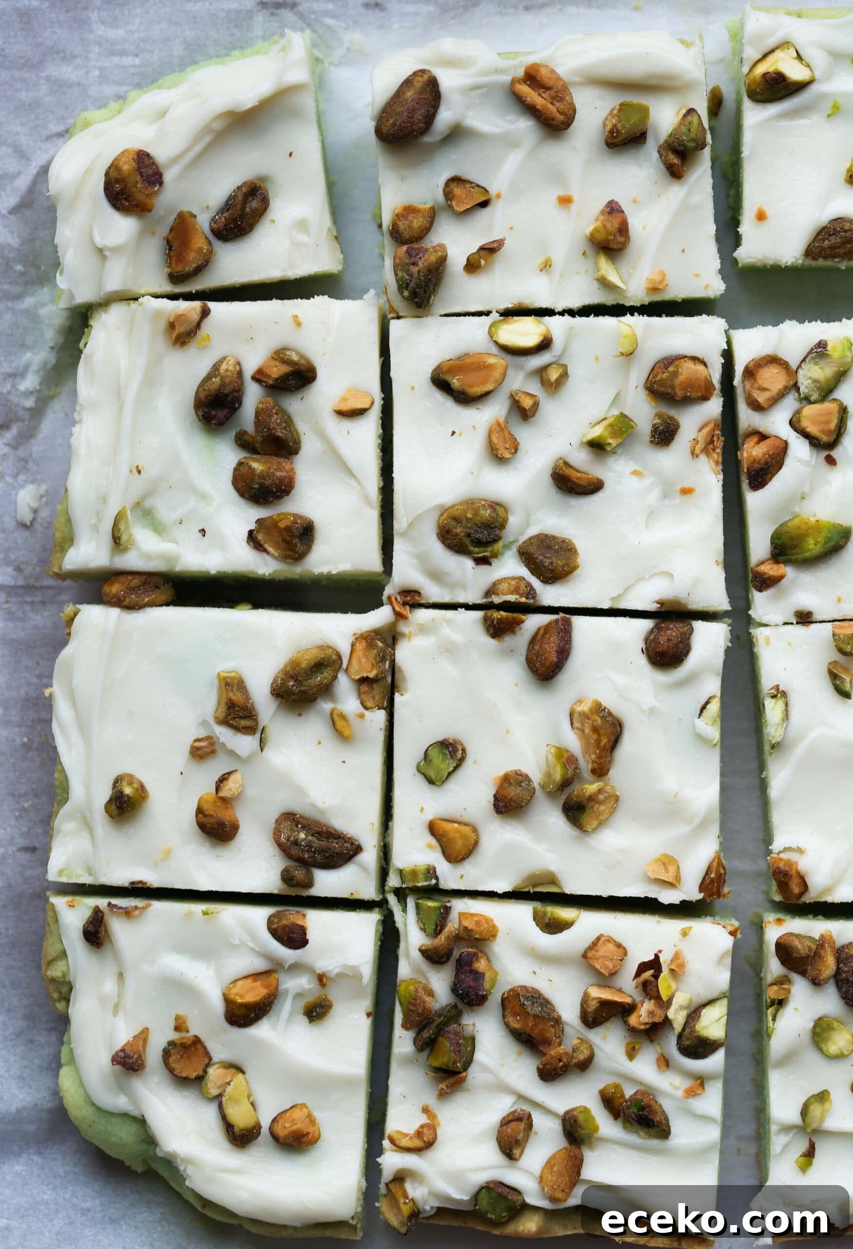 Pistachio Bars topped with cream cheese frosting and chopped pistachios cut on a serving plate from above.