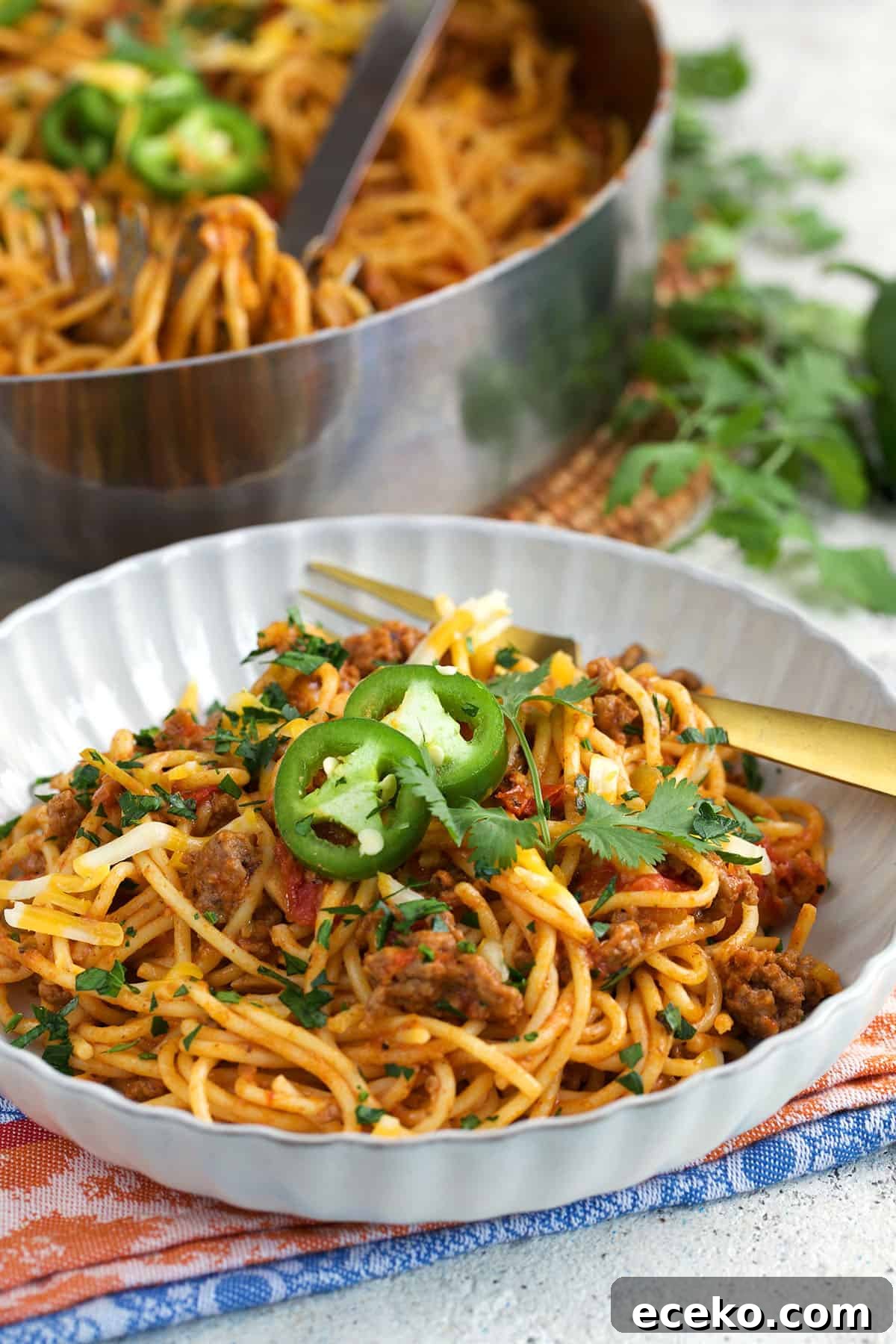 Taco Spaghetti Recipe: Spicy Mexican-Italian Fusion Pasta 2 Taco Spaghetti in a white bowl with a gold fork and a skillet in the background.