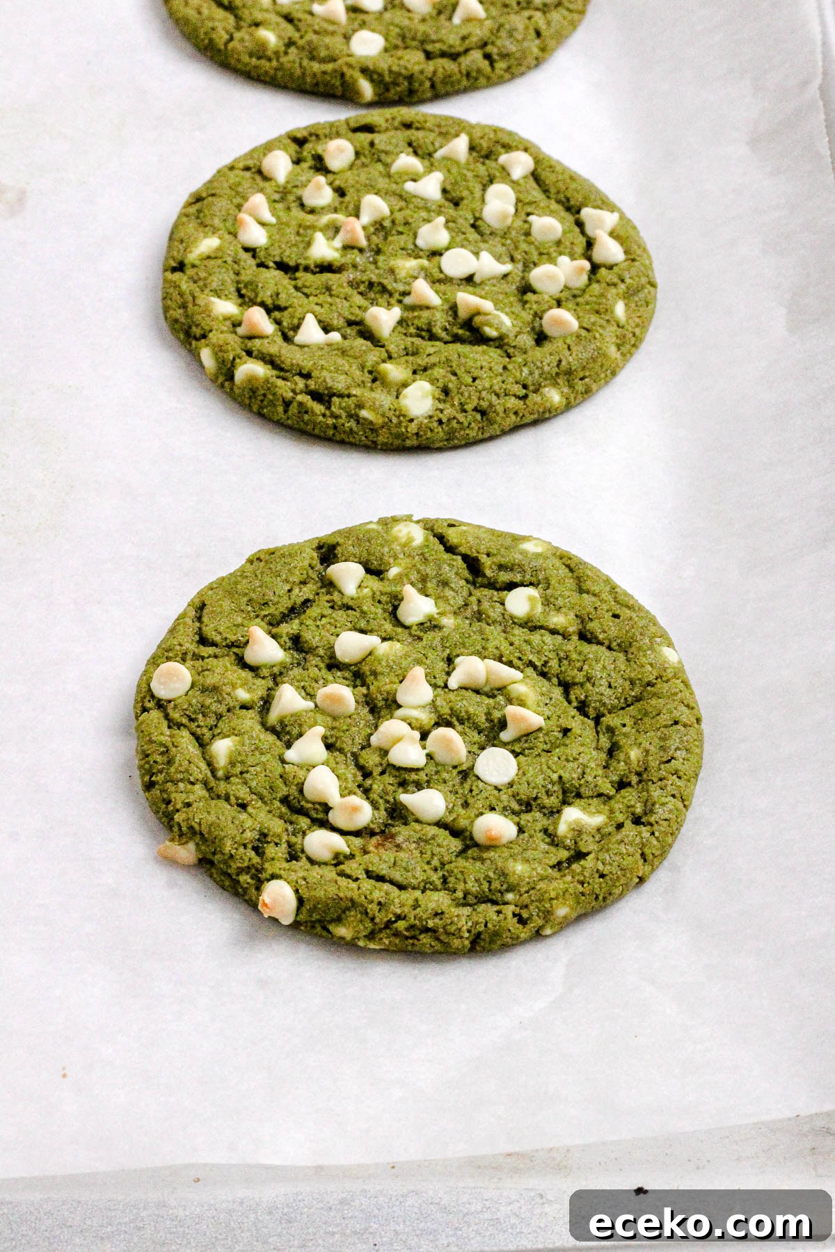 Matcha cookies with white chocolate chips on a parchment lined baking sheet.