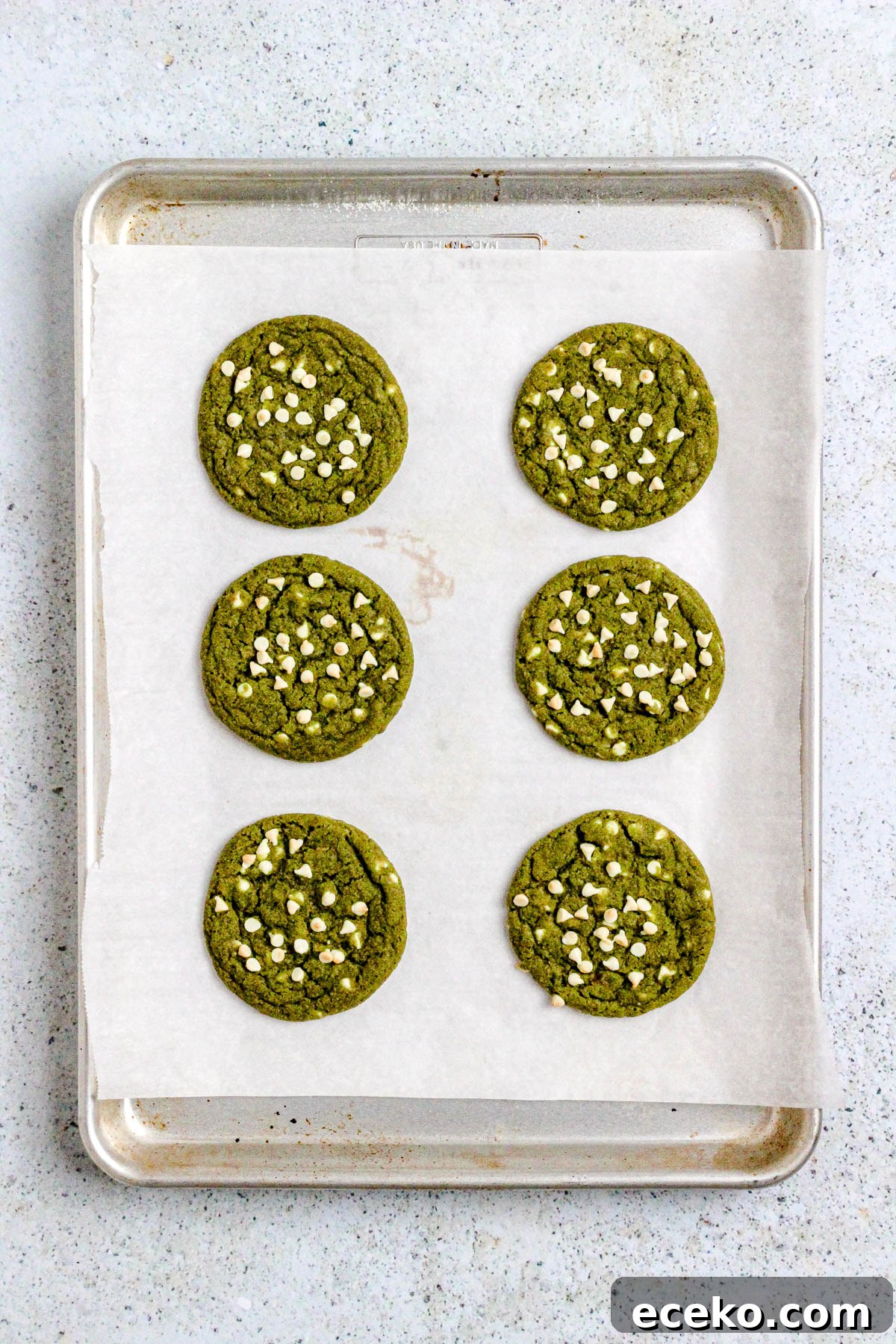 Matcha cookies with white chocolate chips on a parchment lined baking sheet.