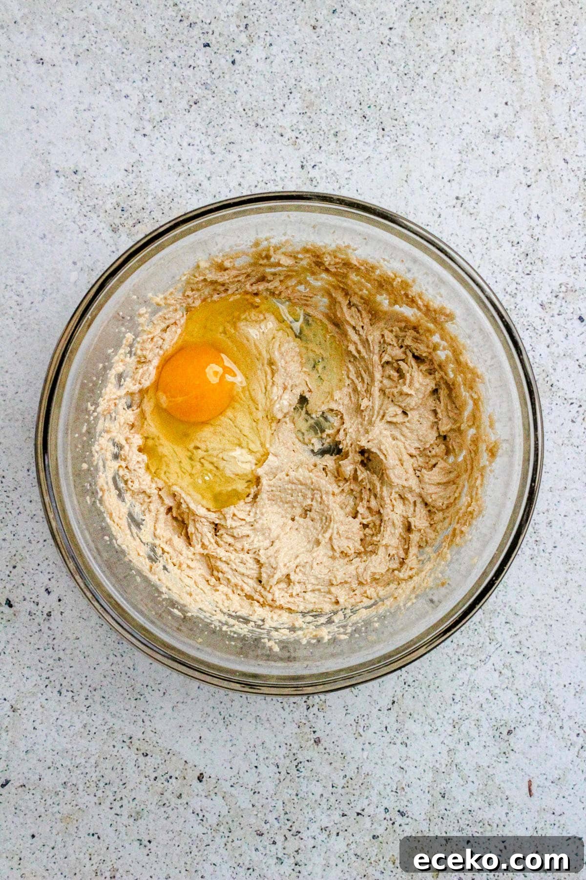 A glass bowl with creamed butter and sugar and an egg.