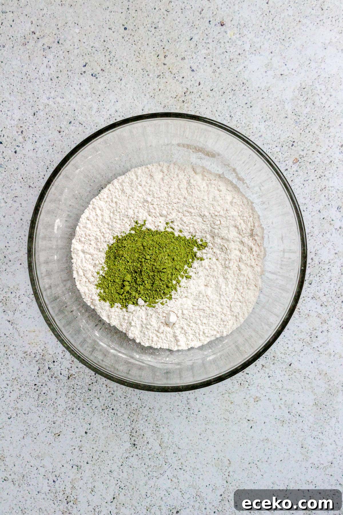 A glass bowl with flour and matcha powder for matcha cookies.