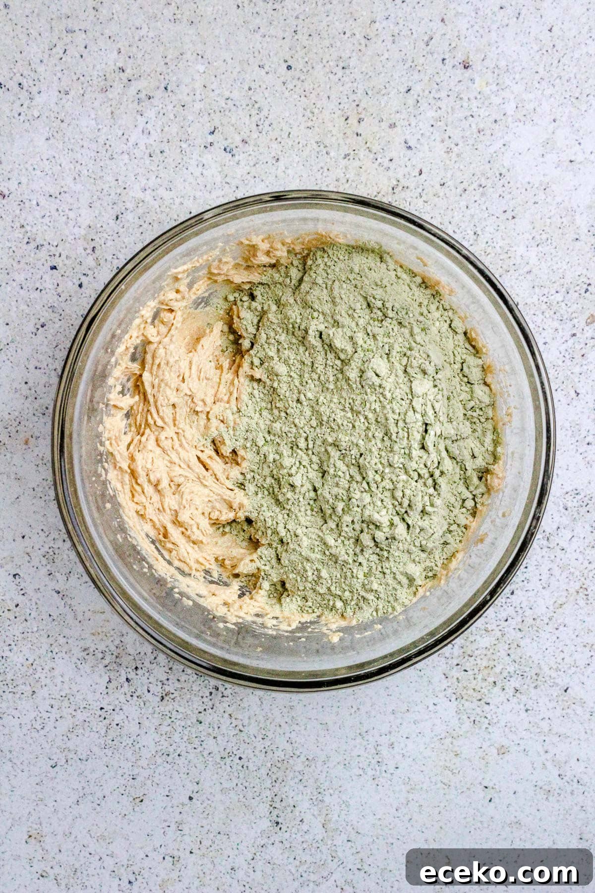 A glass bowl with flour, matcha powder and creamed butter and sugar for matcha cookies.
