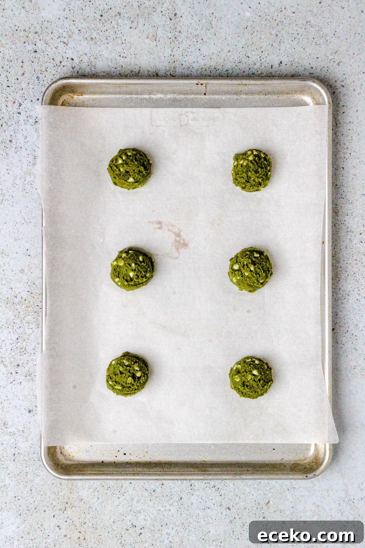 Matcha white chocolate chip cookie dough scoops on a baking sheet.
